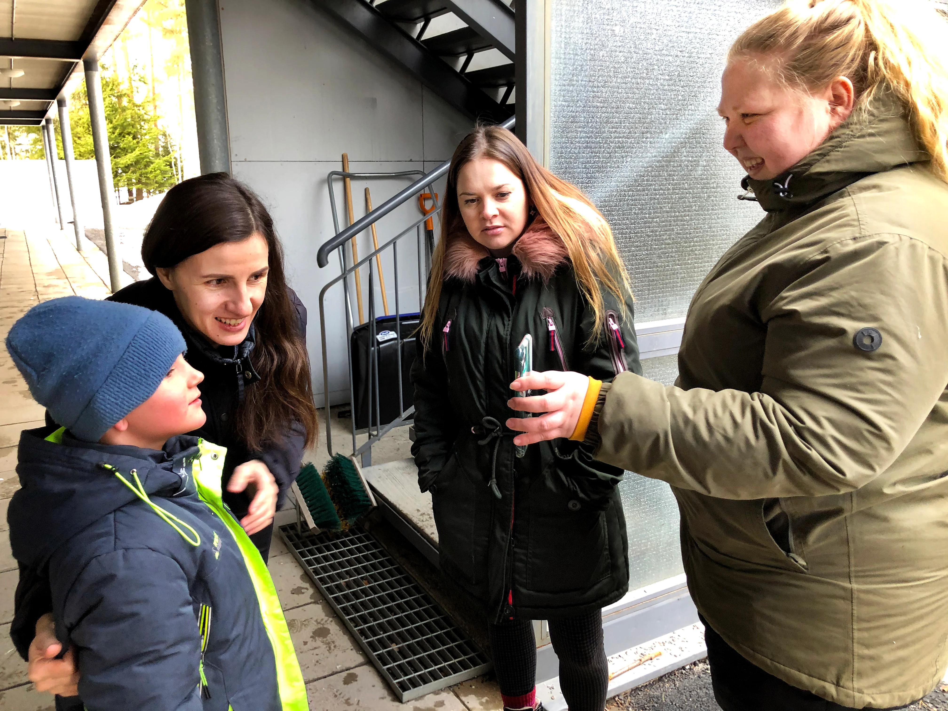 Liliia Marchenko katsoo Yaroclay-poikansa kanssa matkapuhelimen kuvasta millainen kirjoituspöytä Heidi Perkonmäellä (oik.) ja Nataliia Maksimchukilla olisi mahdollisuus tuoda illan seuraavassa kuormassa.