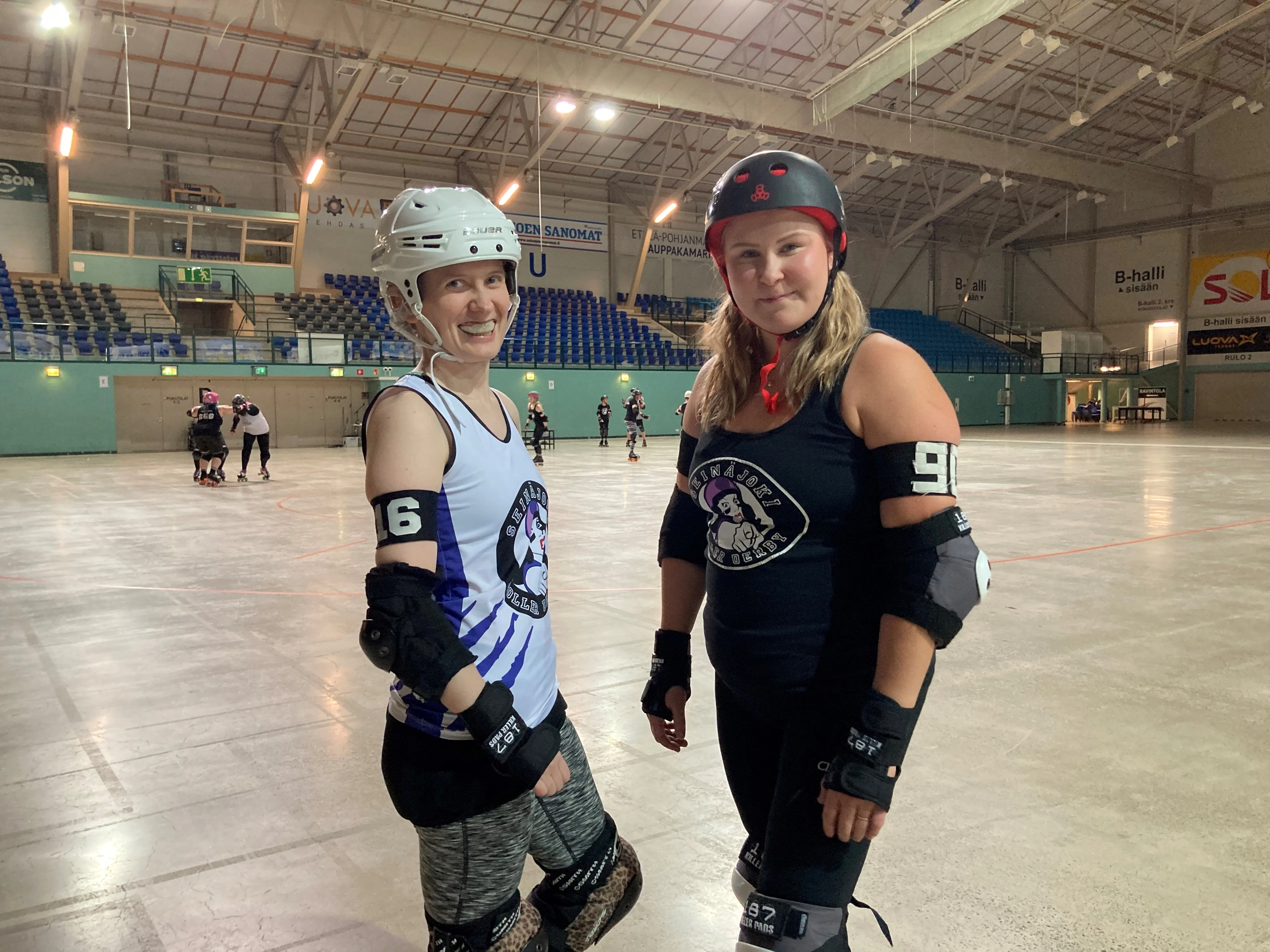 Jenni Siro (vas.) ja Pauliina Korpi poseeraavat pelivarusteissa ja hammassuojissa Seinäjoki Areenan kentällä. Violetti, musta ja valkoinen ovat paikallisen Roller derby -seuran tunnusvärit.