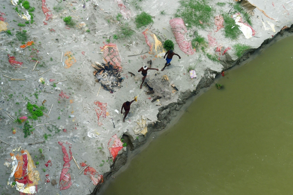 Intiassa Ganges-joki tulvii ja on huuhtonut esille satoja rannoilleen haudattuja koronauhreja. Kuvassa kalastajat kävelevät hautojen seassa. LEHTIKUVA/AFP