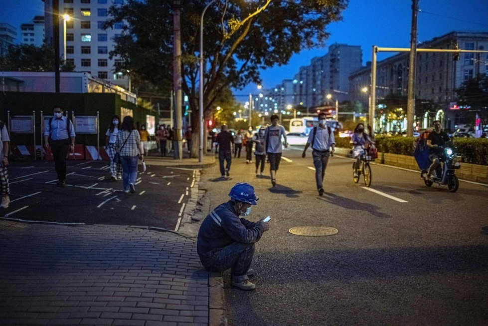 Jalkakäytävän edustalle istunut kansalainen tutki keskittyneesti matkapuhelintaan Pekingin iltaruuhkassa viime syyskuussa.