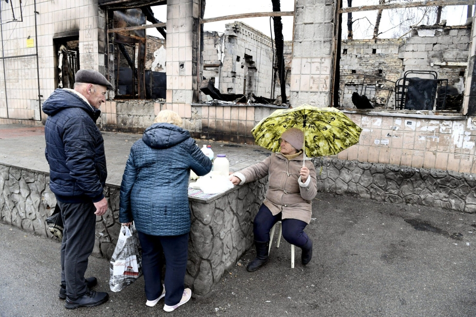 Tetiana Koronik (oik.), 70, myy maitoa ja juustoja tuhoutuneen rakennuksen edustalla Makarivin torilla Ukrainassa 20. huhtikuuta 2022. LEHTIKUVA / JUSSI NUKARI