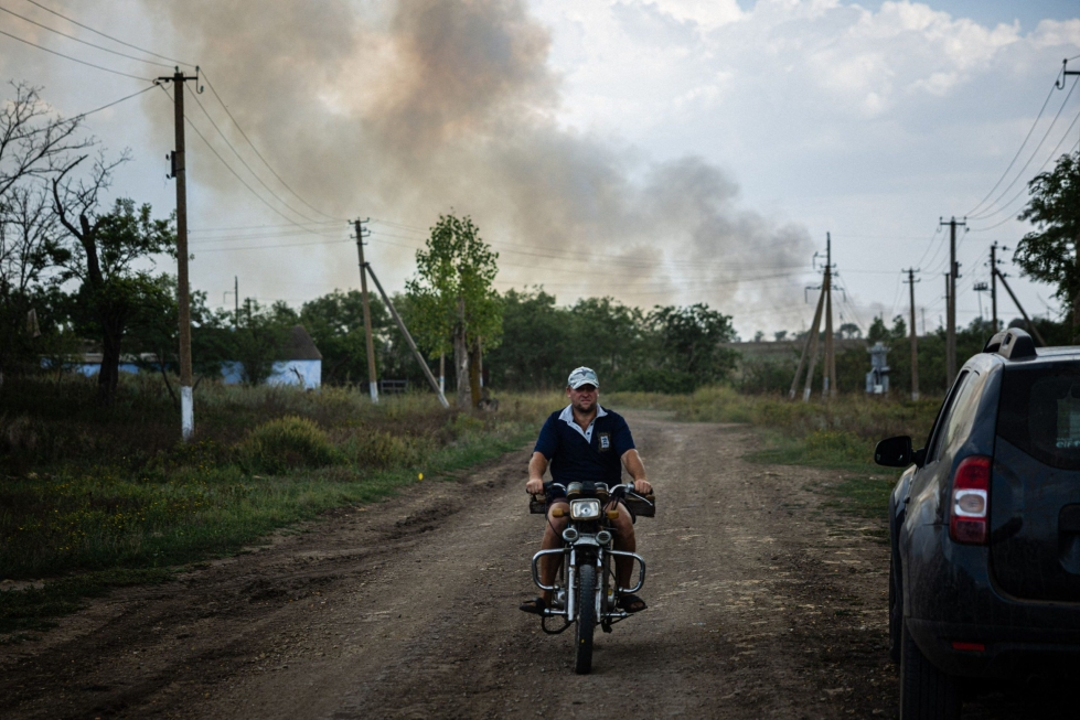 Moottoripyörällä liikkuva mies 30. elokuuta Mykolajivin alueella Ukrainassa lähellä etulinjaa, josta kohoaa savua. AFP/Lehtikuva