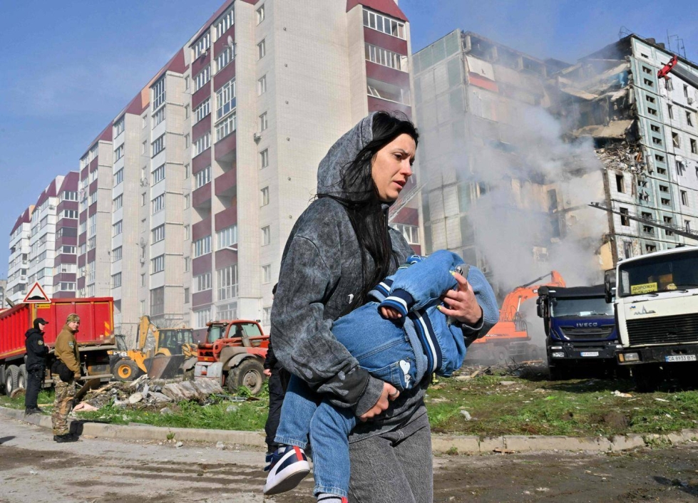 Nainen kävelee lapsi sylissään iskussa vaurioituneen asuinrakennuksen edustalla Umanin kaupungissa.