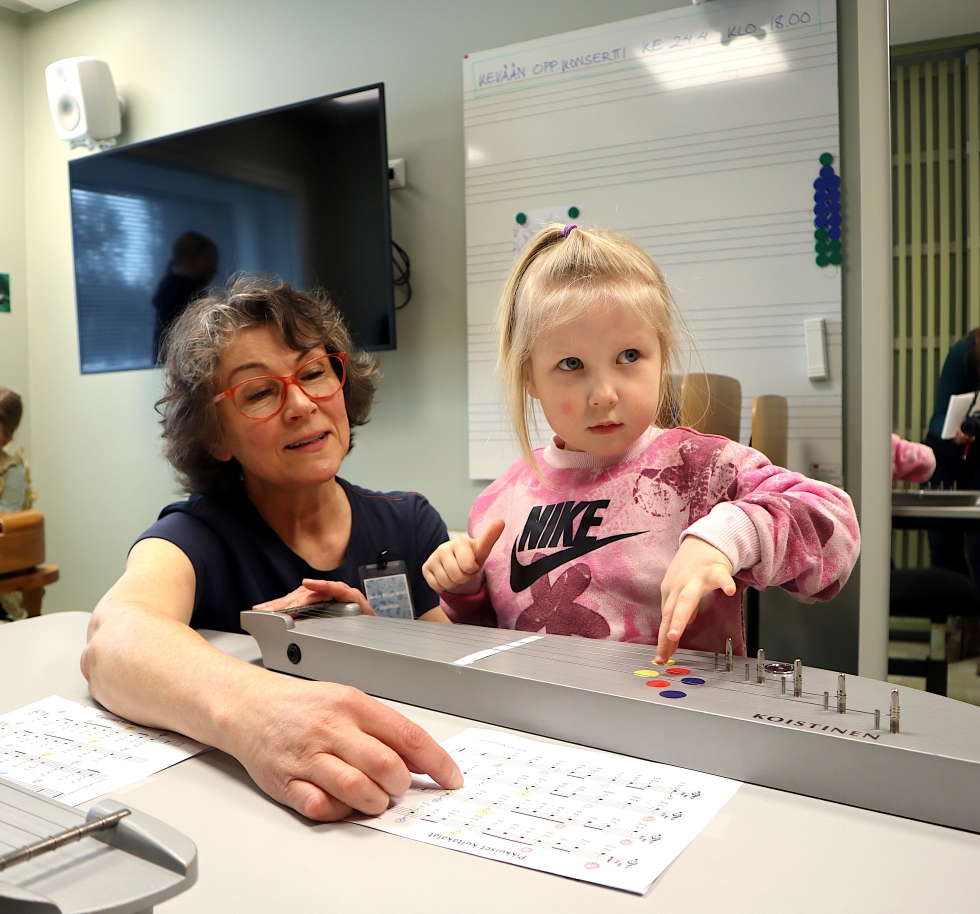 Nelvuotias Isla Saastamoinen kokeilee kanteleen soittamista Anna-Maija Kekin opastuksella.