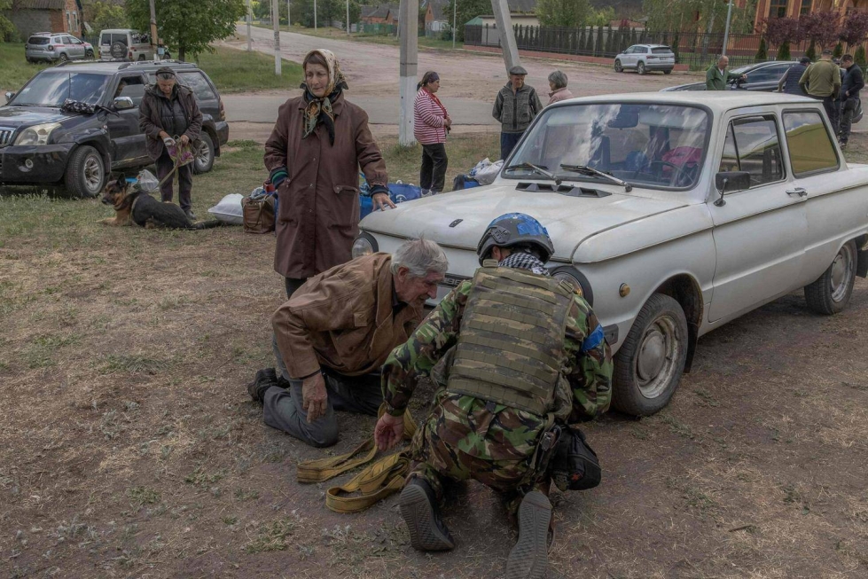 Ukrainalaissotilas auttaa ikääntynyttä pariskuntaa evakuoitumaan Koillis-Ukrainassa sijaitsevasta Lyptsin kylästä.