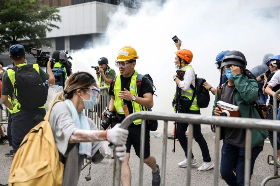 Keskiviikkona Hongkongissa otetussa valokuvassa mielenosoittajia ja median edustajia, jotka reagoivat poliisin käyttämään kyynelkaasuun. LEHTIKUVA/AFP