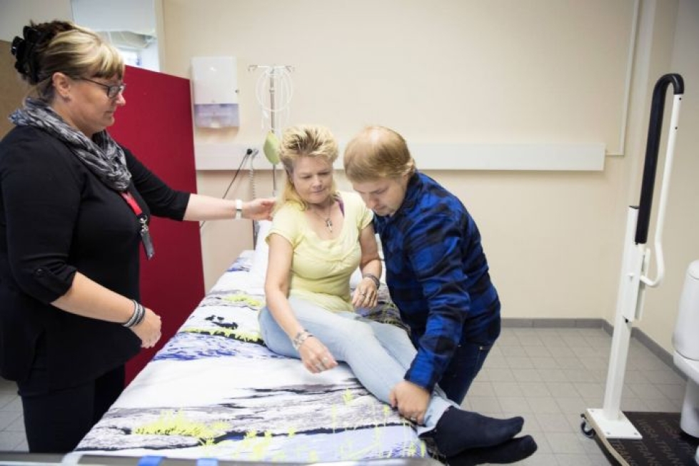 Mika Muhonen näyttää opiskelukaverinsa Maarit Nevalaisen kanssa, kuinka avustettava autetaan ylös sängystä. Opettaja Susanna Puustinen muistuttaa vieressä ergonomisesta työasennosta.