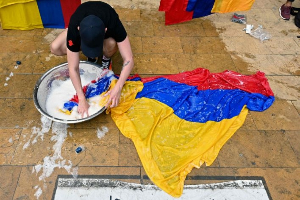 Mielenosoittaja pesee Kolumbian lippua Medellinissä protestina Ivan Duquen hallinnon suunnitelmille. LEHTIKUVA/AFP