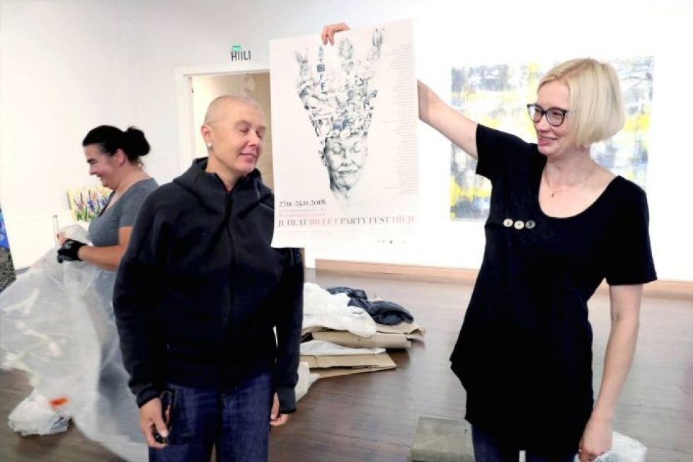 Kuvataiteilija Laura Melkinen (oik.) tarkistaa, onko SKjL:n julisteessa käytetty mallina toiminnanjohtaja Merja Puustista. Taustalla näkyvä Reetta Gröhn-Soininen on yksi juhlanäyttelyn taiteilijoista.