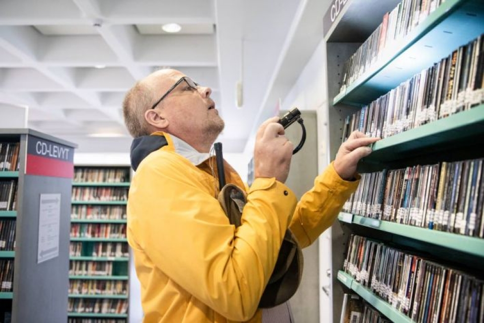 Pekka Makkonen etsii taskulampun avulla itselleen mieluisaa kuunneltavaa kirjaston musiikkihyllystä.