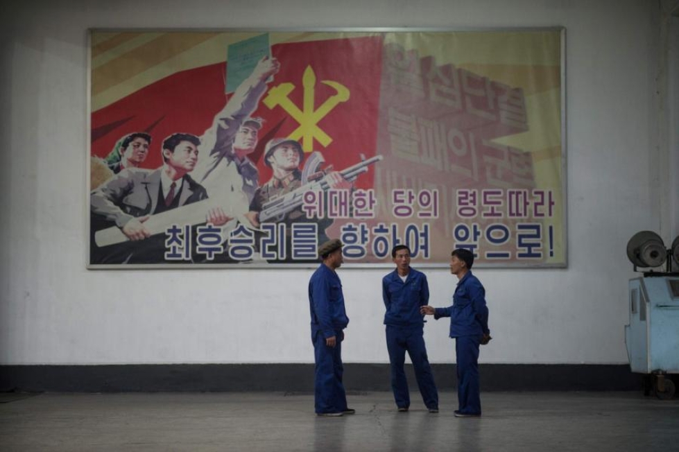 Työntekijöitä seisomassa Pohjois-Koreassa kommunistipuolueen propagandajulisteen edessä sähkökaapelitehtaalla Pjongjangissa. LEHTIKUVA/AFP